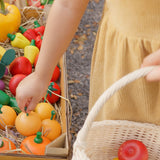Child reaching out for a wooden toy orange from the Plan Toys Fruit Produce Set. She's holding a basket in one hand that's filled with play food - Apples, Oranges & Bananas