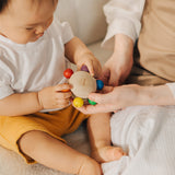 An adult handing the Plan Toys Pull & Grasp wooden baby toy to a baby.