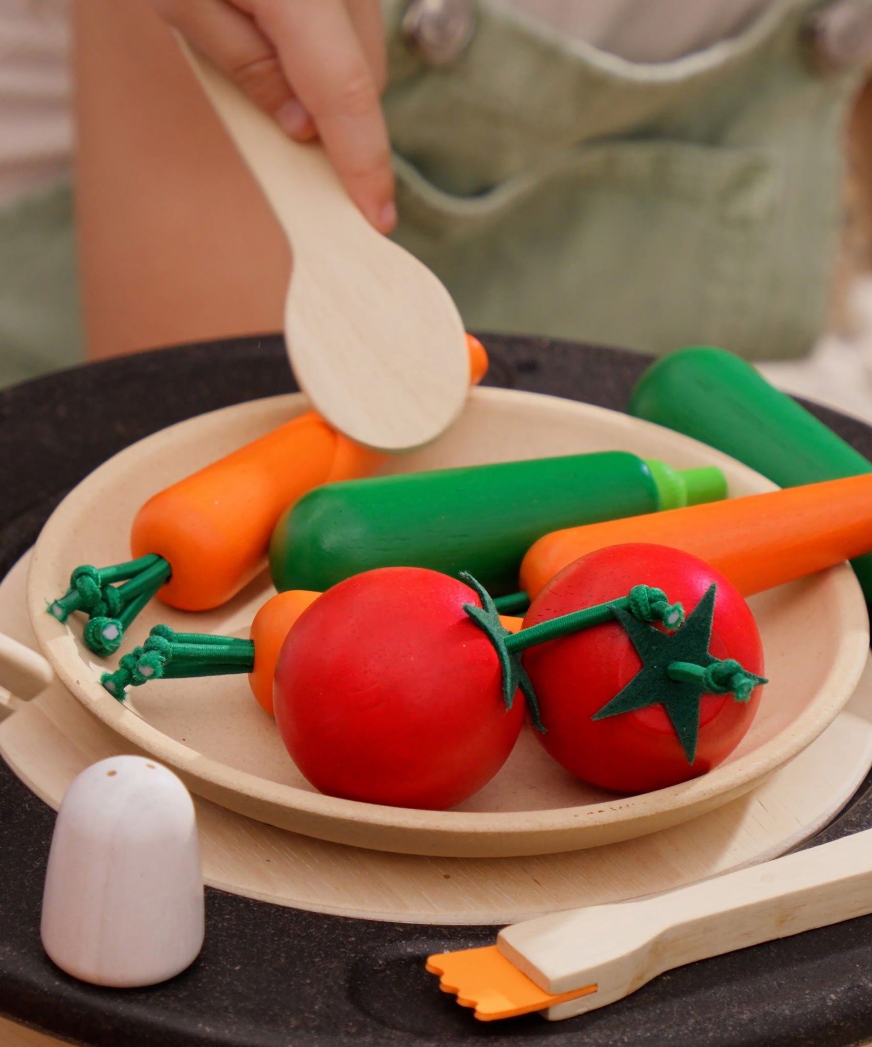 The Plan Toys Vegetable Produce Set with wooden Carrots, Courgettes & Tomatoes play food shown on a wooden toy plate in a play kitchen.