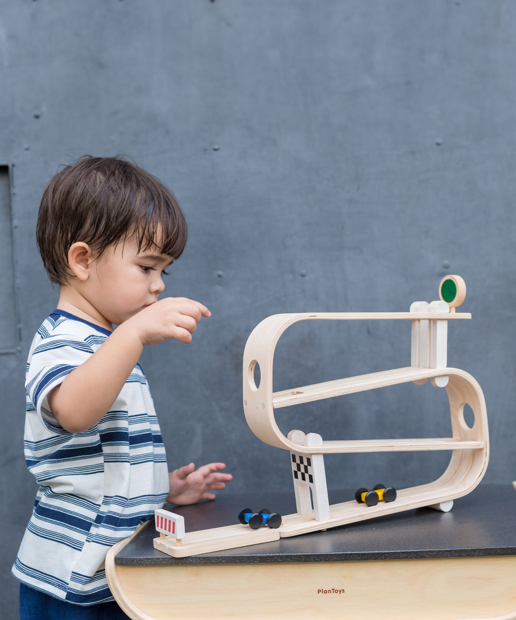 A child playing with the PlanToys Ramp Racer. The ramp racer has been placed on a PlanToys table.