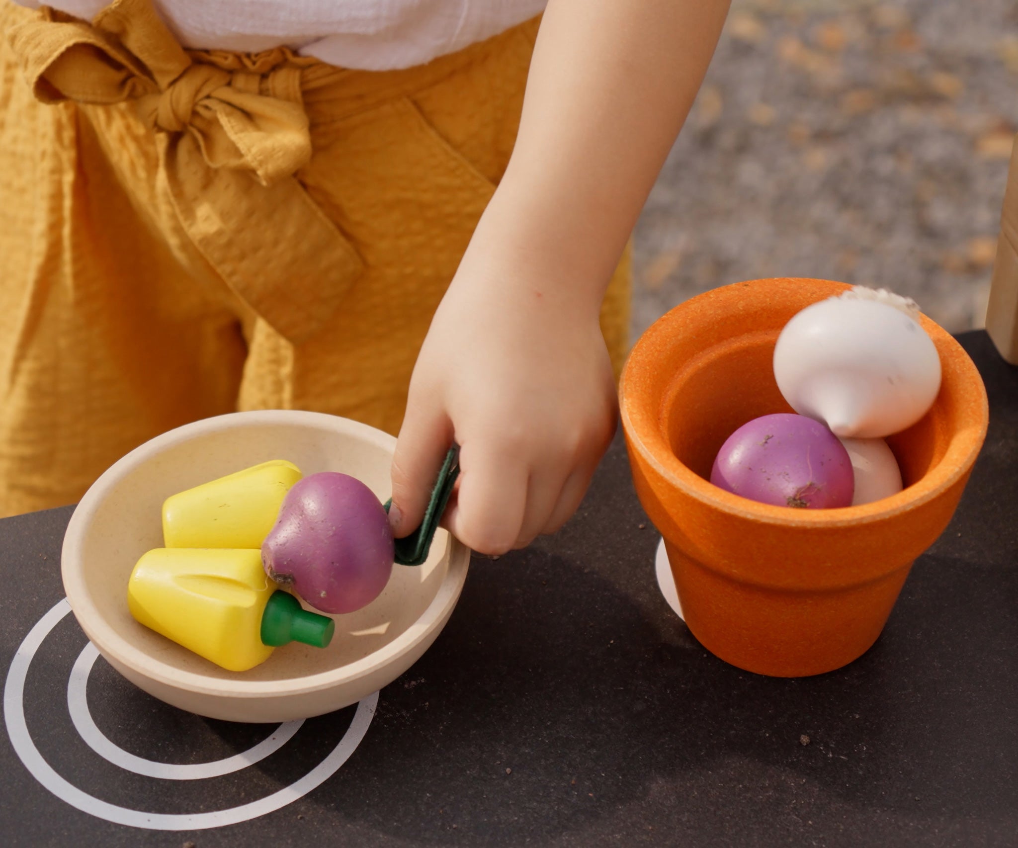 Plan Toys wooden play food Produce Set containing Radish, Garlic & Yellow Peppers. The produce has been placed in a wooden pot and a wooden bowl.