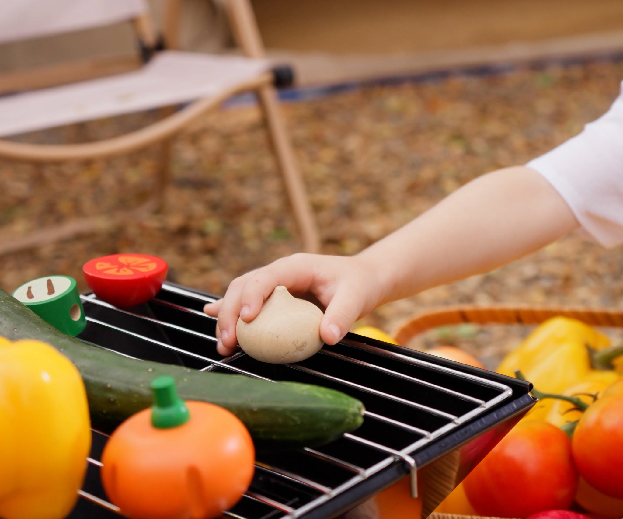 A child placing a toy wooden onion from the Plan Toys Vegetable Produce Set on a metal grill.