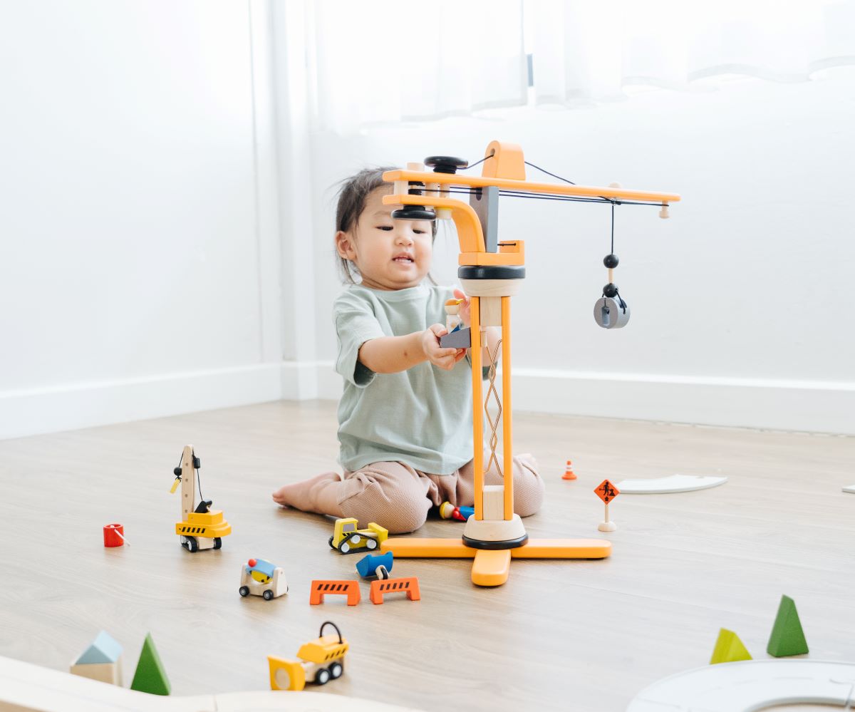 A child sitting on the floor playing with the PlanToys PlanWorld Crane Set.