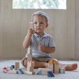 A child playing with the PlanToys Creative Blocks in the Orchard colour way. The child is sitting on a rug.