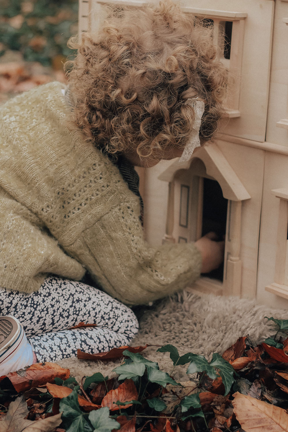 A close up of a child playing with the PlanToys Victorian Dolls House in a forest.