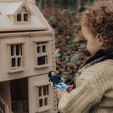 A child playing with the PlanToys Victorian Dolls House in a forest. They are holing onto a wooden dolly.