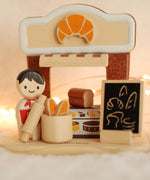 The PlanToys rubber wood bakery and baker, in warm lighting.