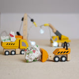 The PlanToys PlanWorld Construction Vehicles Set placed on a light coloured rug, the dozer is pushing a rolled up ball of paper along and the dumper has a piece in it's trainer.