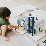 A child crouching down playing with the PlanToys PlanWorld Central Station Wooden toy on a rug.