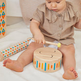Close up of young child playing with the PlanToys solid wooden drum toy on a white blanket