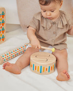 Close up of young child playing with the PlanToys solid wooden drum toy on a white blanket
