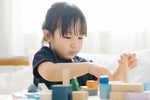 Close up of a young girl playing with the PlanToys plastic-free urban city blocks on a white table
