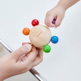 Two hands pulling at the beads of the Plan Toys Pull & Grasp wooden baby toy.