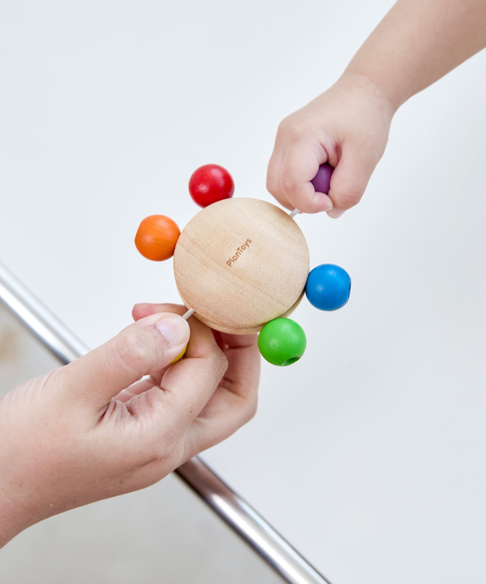 Two hands pulling at the beads of the Plan Toys Pull & Grasp wooden baby toy.