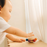 A baby reaching for the Plan Toys Wooden Pull & Grasp Baby Toy.