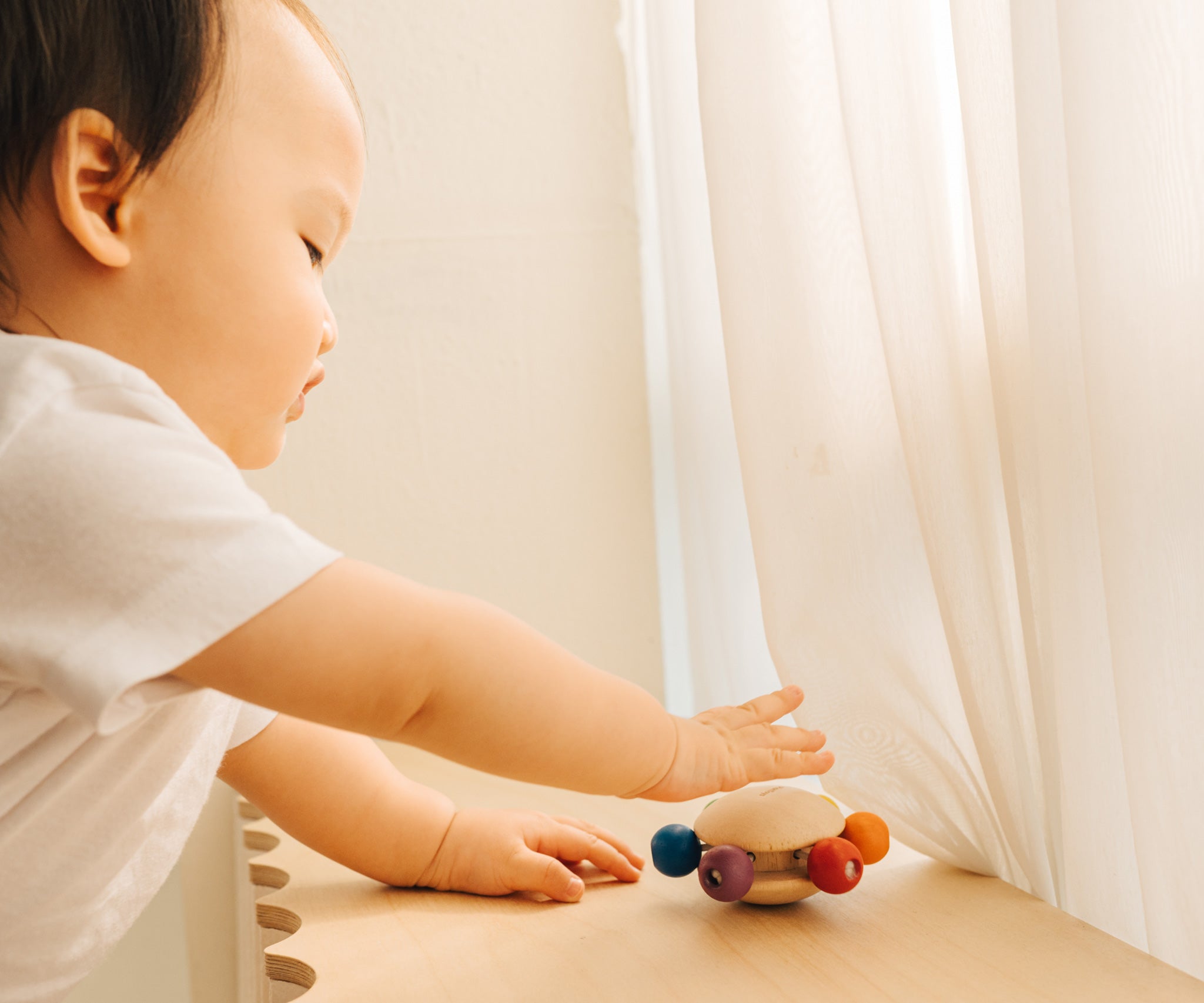 A baby reaching for the Plan Toys Wooden Pull & Grasp Baby Toy.