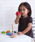 A child playing with the PlanToys Stacking Ring, the child is holding the red ball piece that sits on top of the rod.