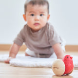 A baby crawling towards the Plan Toys Bird Roller - a rocking baby toy made from rubberwood.