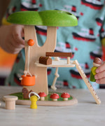 A close up of the PlanToys PlanWorld Tree House being played with by a child. The child's hand can be seen holding onto the little wooden doll figure.