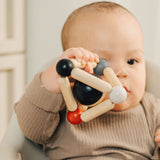 A baby clutching onto the PlanToys high contrast Triangle baby Clutching Toy. A black and natural wood wooden ball in a stretchy triangle clutching toy. PlanToys range of toys are made from sustainably sourced rubberwood, we're proud stockists of PlanToys here at Babipur.