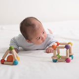 A baby is laying on his front on a bed with PlanToys Triangle and cube Clutching Toys in front of them.