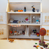 A PlanToys Victorian dolls house with furniture inside, decorated for Halloween, with paper pumpkin bunting made with the Babipur Pumpkin tape.