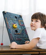 A child laying in front of a the PlanToys Wall Ball Game. The child has decorated the board with drawings.