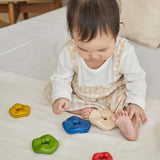 A baby playing with the Plan Toys wooden Wave Stacker - a tactile stacking rainbow baby toy.