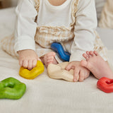 A close up of a child's hands playing with the Plan Toys Wave Stacker - a wooden stacking baby toy in rainbow colours.