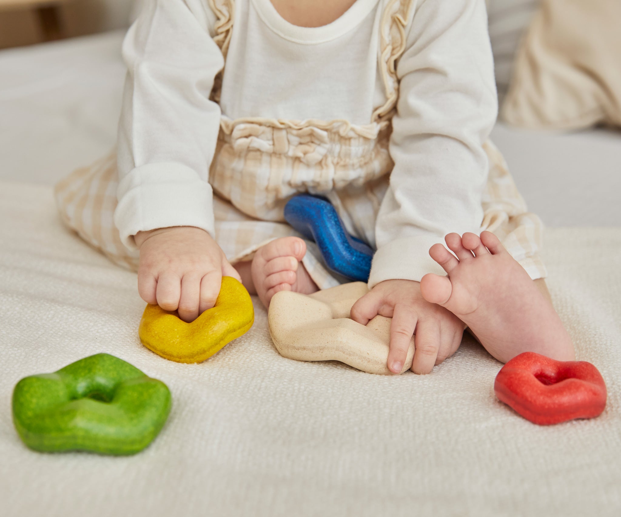 A close up of a child's hands playing with the Plan Toys Wave Stacker - a wooden stacking baby toy in rainbow colours.