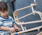 A child playing with the PlanToys Ramp Racer. The ramp racer has been placed on a PlanToys table. The child is holding the red and yellow cars.