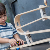 A child playing with the PlanToys Ramp Racer. The ramp racer has been placed on a PlanToys table. The child is holding the red and yellow cars.