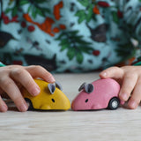 A close up of the PlanToys Wooden Pull-Back Mouse Toys in yellow and pink in a child's hands.