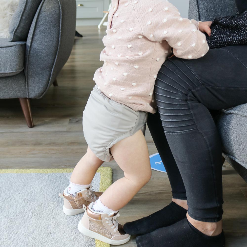 A baby wearing The Close Pop-In reusable cloth nappy with adjustable velcro, in Cloud Grey.