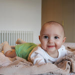 A baby on a bed, wearing The Close Pop-In reusable cloth nappy with adjustable velcro, in mint green