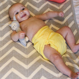 A baby on a bed, wearing The Close Pop-In reusable cloth nappy with adjustable velcro, in sunshine yellow