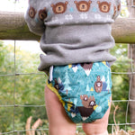 A baby wearing the Close Pop-In +bamboo reusable cloth nappy with adjustable velcro closures, in a bear print