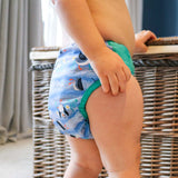 A baby wearing The Close Pop-In +bamboo reusable cloth nappy with adjustable velcro closures, in a puffin print