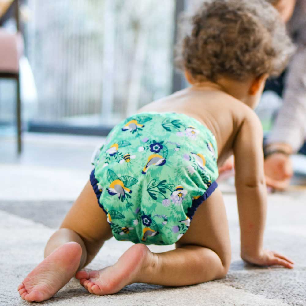 A baby wearing The Close Pop-In +bamboo reusable cloth nappy with adjustable popper closures, in a round the garden birds print