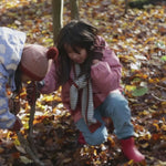 Child playing in a forest wearing a Warm and Waterproof (5000M rating), PVC free kids Winter school coat by Little Green Radicals, in pink coral, with red front pockets, available to buy at Babipur.
