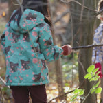Girl roaming around a forest wearing a Warm and Waterproof (5000M rating), PVC free kids school coat by Little Green Radicals, in a floral Winter Rabbit print in turquoise, available now at Babipur.