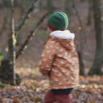 Boy running around a forest wearing a Little Green Radicals Kids Warm Waterproof Winter School Coat in a gold yellow duck print, with a cosy lined hood, for sale at Babipur.