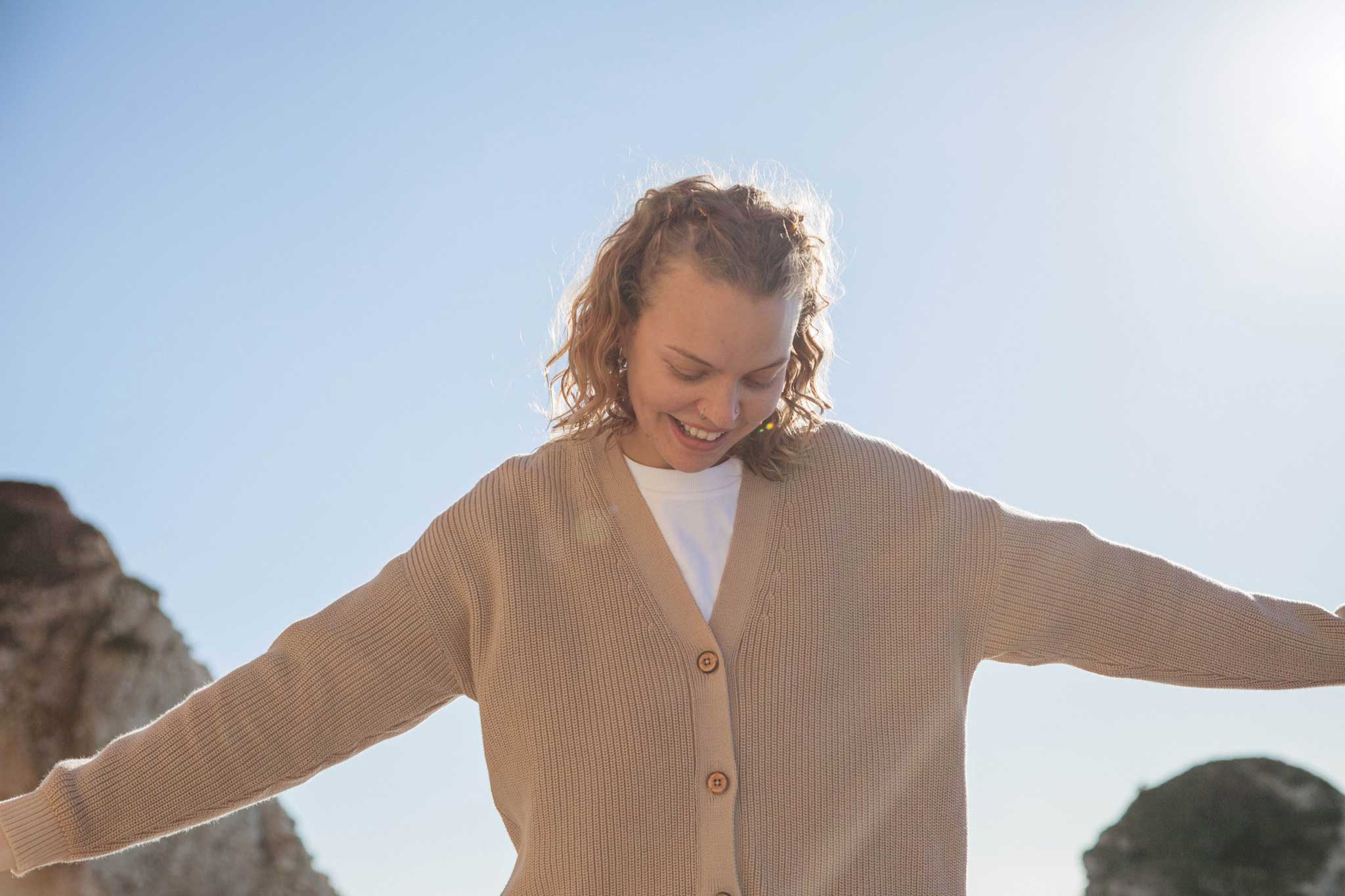 A woman wearing the Rapanui Brook Organic Cotton Women's Knitted Cardigan. The woman has her arms stretched out.