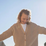 A woman wearing the Rapanui Brook Organic Cotton Women's Knitted Cardigan. The woman has her arms stretched out.