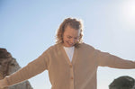 A woman wearing the Rapanui Brook Organic Cotton Women's Knitted Cardigan. The woman has her arms stretched out.