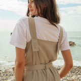 A close up of the driftwood Rapanui jumpsuit showing the shoulder strap detail with holes for different size adjustments  on organic cotton fabric.