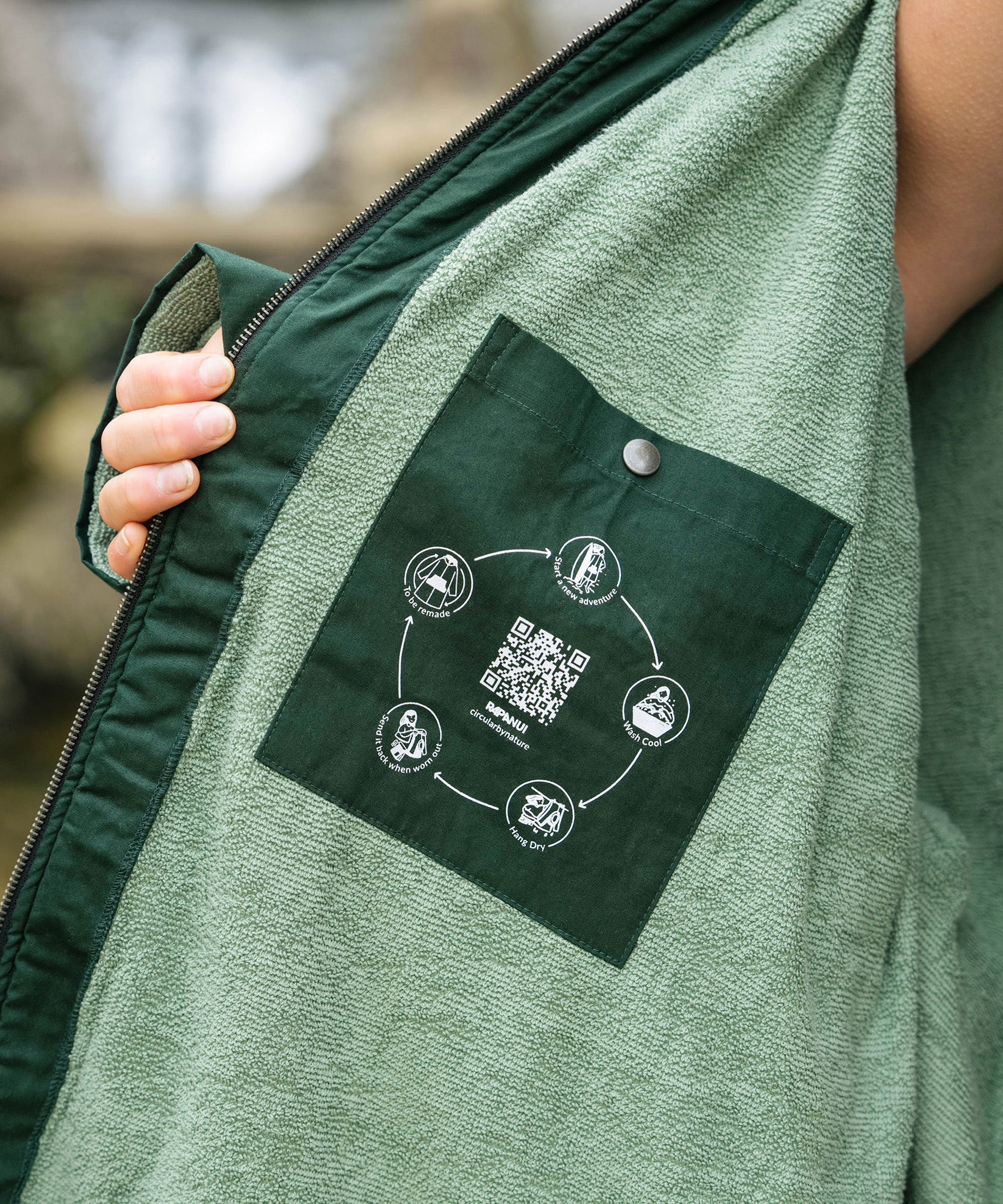 A close up of the inside lining of the Rapanui changing robe in evergreen colour showing the towelling detail on the inside and zip detail. Features a pocket on the inside with washing and drying instructions.