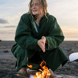 A woman on the beach wearing the Rapanui changing robe in evergreen colour. A organic cotton long length changing robe with PFC-free water-resistant coating