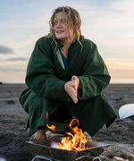 A woman on the beach wearing the Rapanui changing robe in evergreen colour. A organic cotton long length changing robe with PFC-free water-resistant coating