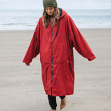 A woman on the beach wearing the Rapanui changing robe in rust colour. A  organic cotton long length changing robe with PFC-free water-resistant coating